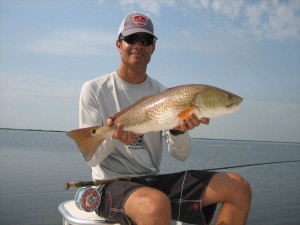 Man in white T shirt proudly shows the fish he caught