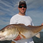 Man in white T shirt poses with the fish he caught