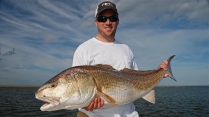 Man in white T shirt poses with the fish he caught