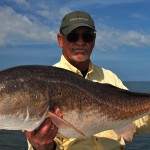 Man in dark cap shows his catch to the camera