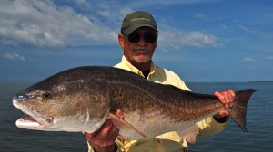 Man in dark cap shows his catch to the camera