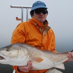 Man in orange jacket and blue cap shows his catch