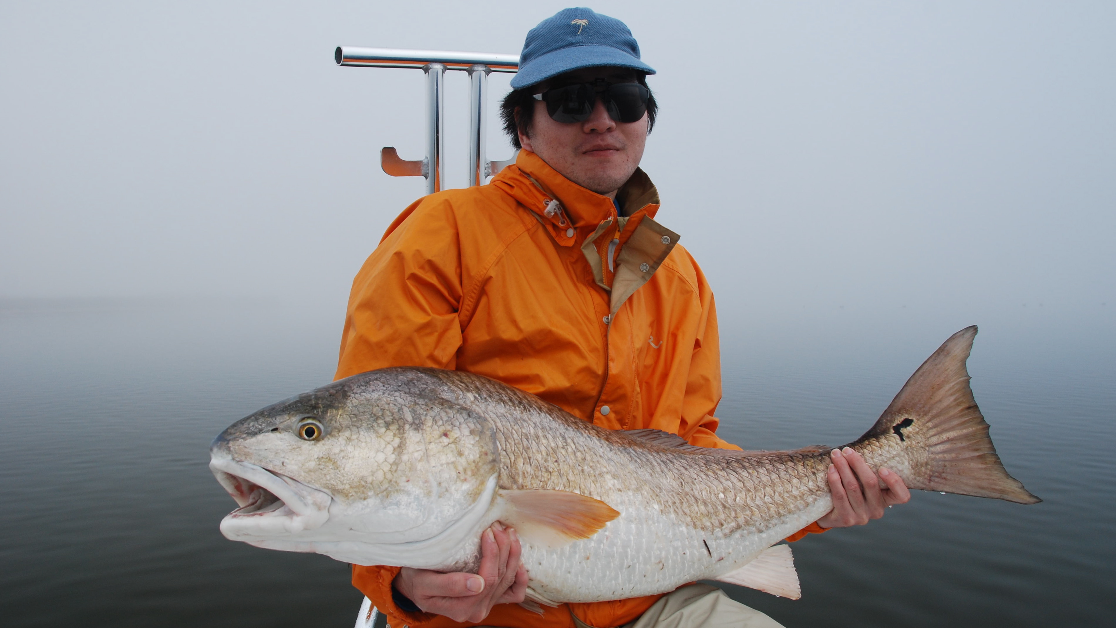 Man in orange jacket and blue cap shows his catch