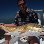 Man in check shirt poses with the fish he caught