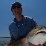 Man in blue shirt poses with the fish he caught