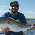 Man in blue jacket poses with the fish he caught