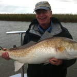 Man in dark colored outfit smiles with the fish he caught