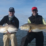 Two men strike a dynamic pose with their fishes