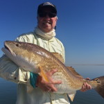 Man in white outfit smiles after catching a fish